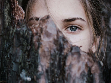 young girl hidden behind a tree. shy and worryed about life with anxiety.